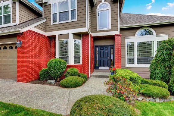 American beige house with red brick trim and dark blue front door. Concrete walkway with nicely trimmed bushes. Northwest, USA