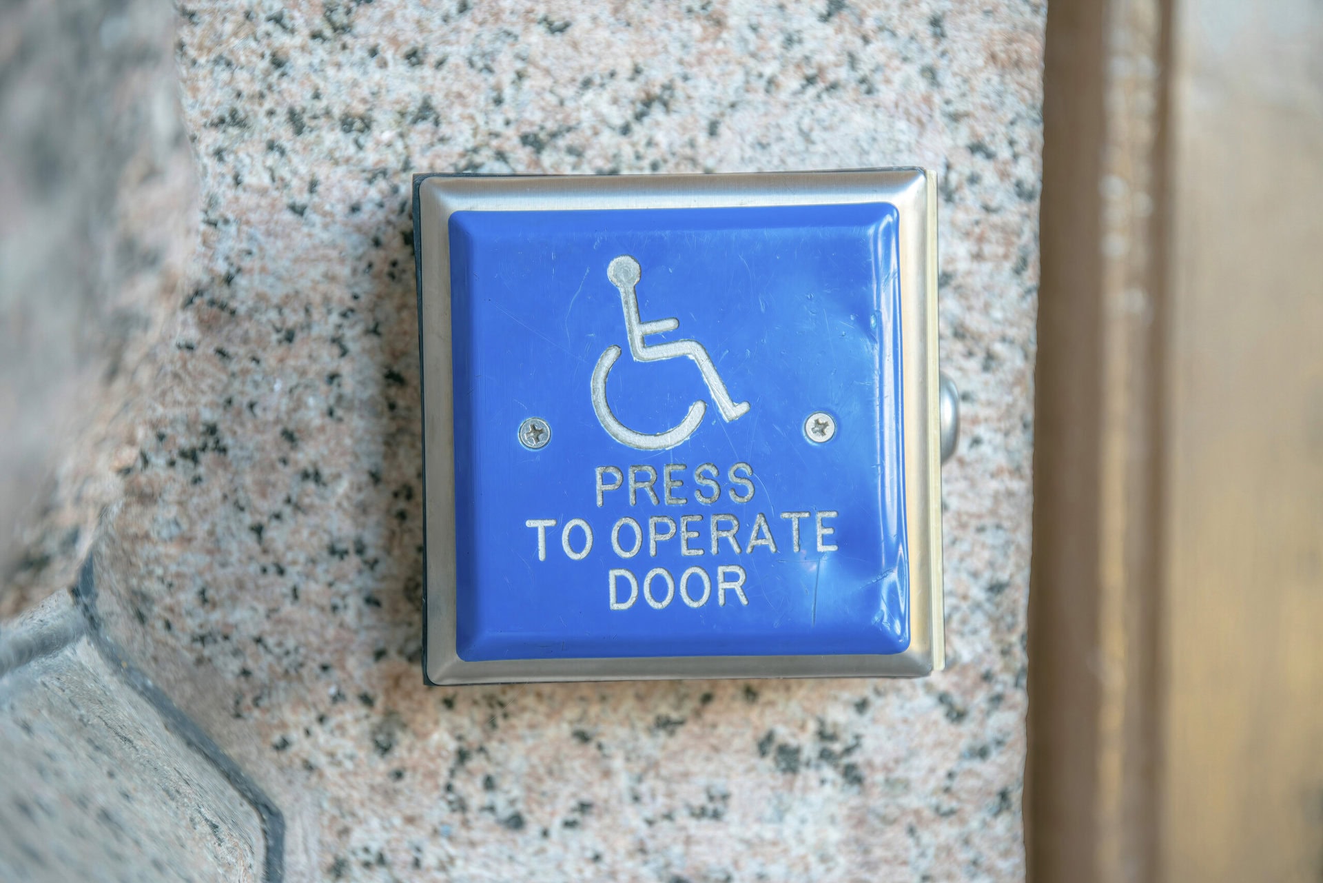 Close up of a blue square electronic button to open entryway for people on wheelchairs.